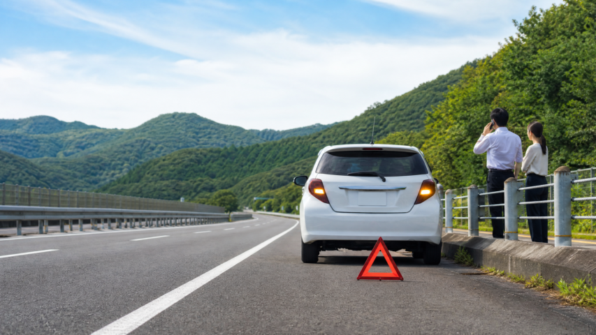 Rental car safely stopped on a Japanese expressway shoulder with warning triangle and travelers behind the guardrail