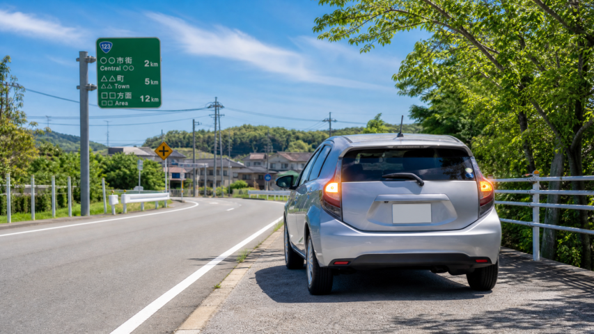 SUV parked on the roadside with brake lights on, green highway sign in the distance under a blue sky with trees nearby