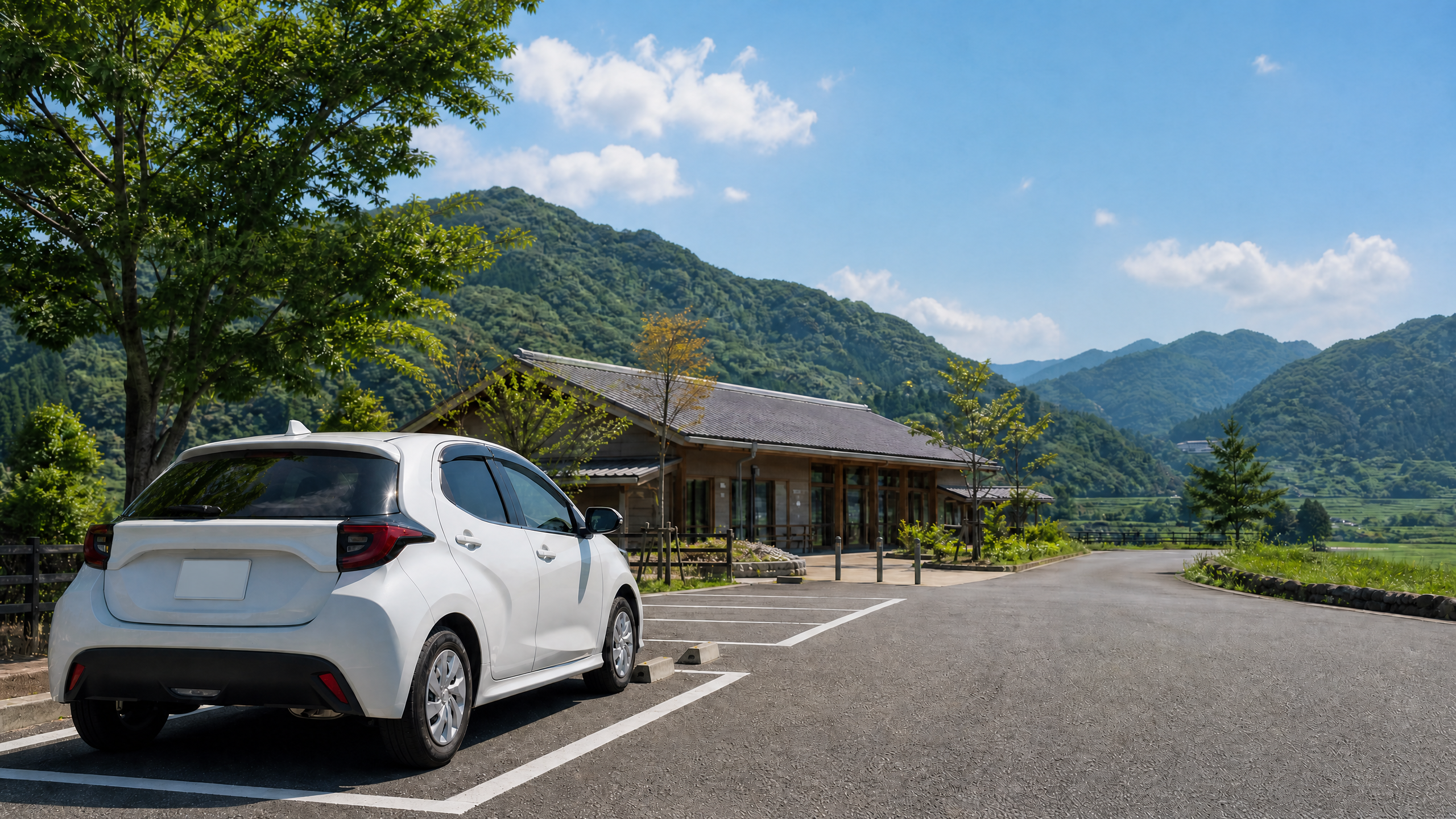 White SUV parked in a parking lot beside a wooden building, with forested hills and a blue sky in the background.