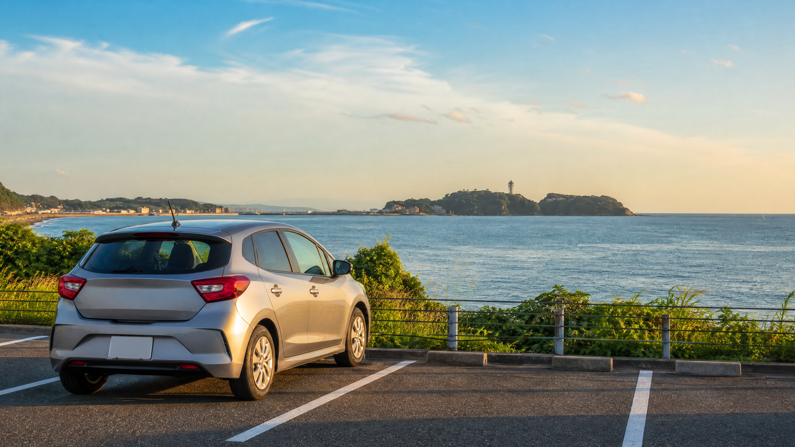 Silver compact car parked in a seaside parking lot with a railing and the ocean behind it.